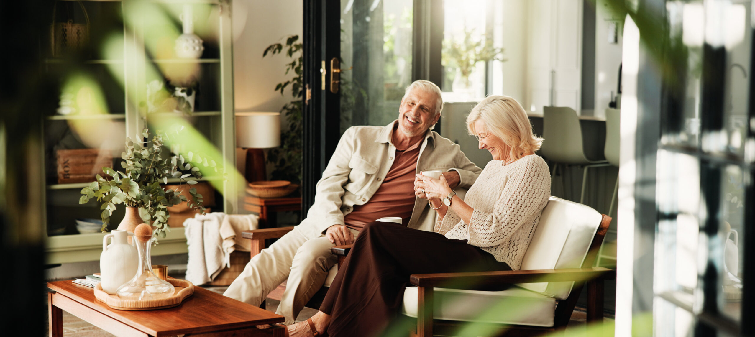 Coffee, laughing and relax with old couple in living room of home together for break or wellness. Drink, funny and love with happy senior people in apartment for bonding, me time or retirement.